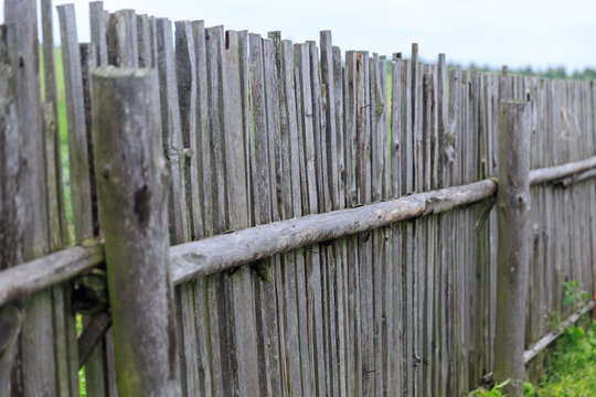 A scratched long old wooden fence in a village with nails in it