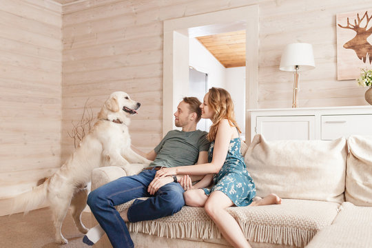 Young Happy Married Couple Nice Girl And Young Man In Casual Clothes Talking With His Kind Obedient Dog In The Living Room Of His Cozy Country House