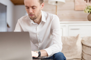 Young male businessman chatting with his colleagues in social networks sitting on the sofa in his designer lounge in the luxury apartment