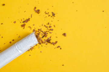 A crumpled cigarette with a row of scattered tobacco on a yellow background. Copy space.