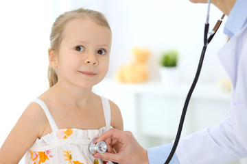 Doctor examining a little girl by stethoscope. Happy smiling child patient at usual medical inspection. Medicine and healthcare concepts