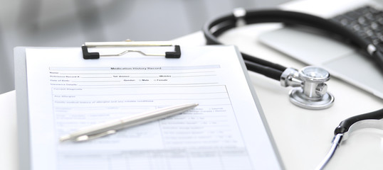 Stethoscope, clipboard with medical form lying on hospital reception desk with laptop computer. Medical tools at doctor working table. Medicine and health care concept