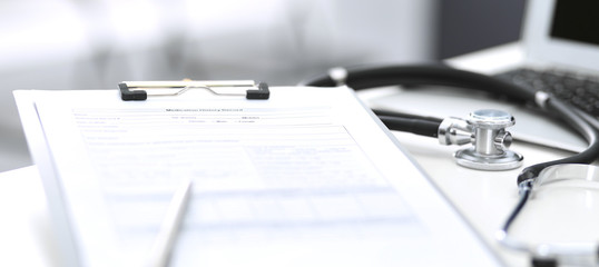Stethoscope, clipboard with medical form lying on hospital reception desk with laptop computer. Medical tools at doctor working table. Medicine and health care concept