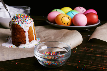 Easter baking with icing and colored powder and eggs. Preparing for the holiday on the kitchen table, on a dark background.