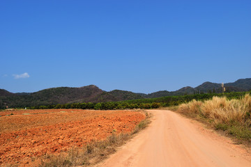 Fototapeta na wymiar Open dirt road in farmland with mountain forest and blue sky in background, The land was plowing and turning over the soil in preparation for planting, Thailand