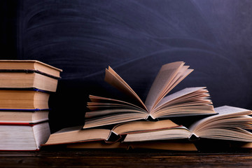 Open books are a stack on the desk, against the background of a chalk board. Difficult homework at...