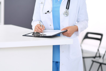 Unknown doctor woman at work, hands close-up. Female physician filling up medical form while standing near reception desk at clinic or emergency hospital. Medicine and healthcare concept