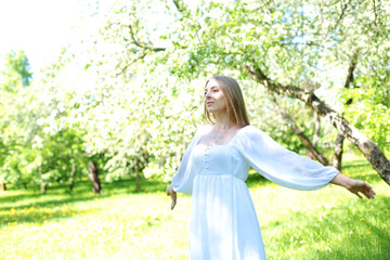 Happy blonde woman on a background of blooming spring garden with her hands raised to the sky