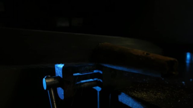 Worker sawing wood in the vise with a hacksaw in the workshop. Blue light