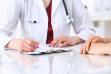 Fototapeta premium Unknown doctor woman consulting patient while filling up an application form at the desk in hospital. Just hands close-up. Medicine and health care concept