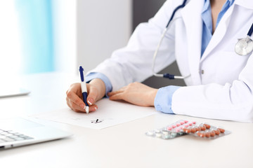 Female doctor filling up prescription form while sitting at the desk in hospital closeup.  Healthcare, insurance and excellent service in medicine concept 