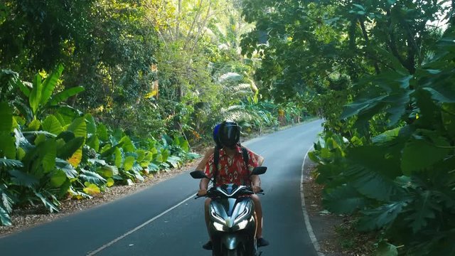 Young beautiful tourist couple rides the jungle on a scooter wearing helmets. Travel, freedom, happiness, vacation, honeymoon concept.