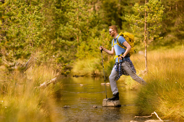 Young man crosses a mountain stream on a sunny day