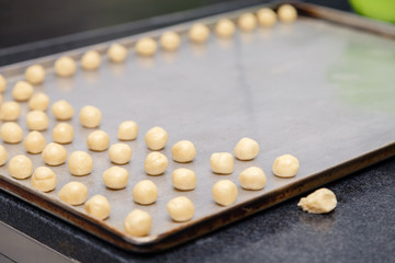 Closeup of a pastry chef at the professional kitchen of the restaurant making shortbread cookies, cutting dough, rolling into small round balls and putting them on a baking sheet with baking paper