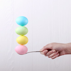 Female hand holds a spoon on which multi-colored eggs are balanced, on a white background. Unusual design, Easter concept, copy space.