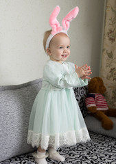 funny little girl in a headband with bunny ears claps her hands and laughs