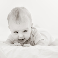 Portrait of beautiful infant baby lying on stomach in bed, black white image with bit toning