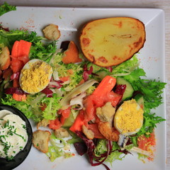 plate of lettuce salad with salmon, mimosa eggs, potatoes and sauce, diet dish