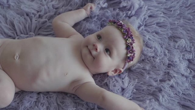 A naked little girl on a photosession on the purple cover smiling in slow motion