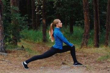 Legs stretching in low lunge. Girl in blue sportswear doing exercises outdoors in coniferous forest. Healthy lifestyle sport concept.