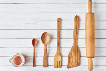 Wooden kitchen utensils on white wooden background with copy space. Spatula, spoons and rolling pin in row, top view