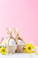 Easter colored eggs with painted faces in paper tray with decorationd on a pink background