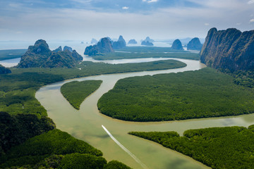 Fototapeta premium Aerial drone view of a small boat on a mangrove forest river heading towards open ocean past towering limestone cliffs and islands