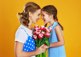 happy mother's day! child daughter   gives mother a bouquet of flowers on color yellow background.
