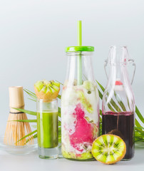 Iced Matcha fusion latte in bottle with ingredients: matcha espresso, red berries juice, kiwi fruits and milk on table with copy space. Healthy summer detox beverage concept. Matcha drink.