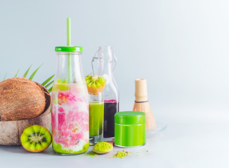 Vegan matcha fusion drink in bottle with ingredients: matcha, red berries juice, kiwi fruits and coconut milk on table with copy space. Healthy detox beverage concept