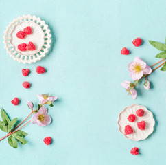 Fototapeta na wymiar Food background with fresh raspberries in white bowls on light turquoise background with flowers, top view with copy space