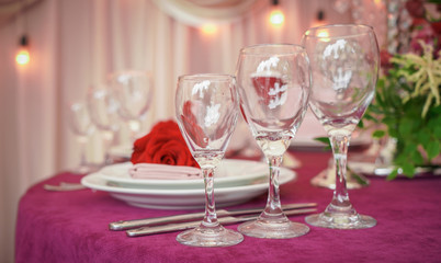 Festive wedding table setting with red flowers, napkins, vintage cutlery, glasses and candles, bright summer table decor.