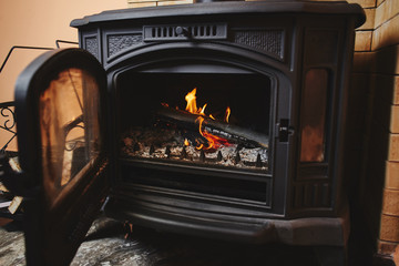 Fireplace of black color with fire burning inside. Stylish interior, giving warmth in the house.