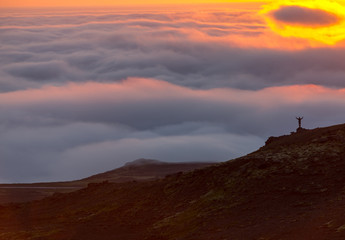 Silhouette of a man on the ridge above the sea of clouds, misty mountains at sunset in Iceland