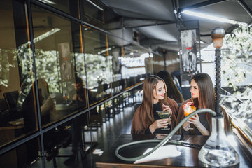 Young beautiful girls are sitting on the summer terrace of a modern cafe and drinking refreshing cocktails in orange and green.