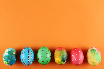 Bunch of colorful tie dye and polka dot painted Easter eggs on bright orange paper background with a lot of copy space for text. Top view, flat lay, close up. Easter greeting card concept.