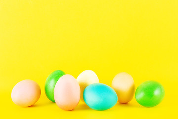 Bunch of blank painted Easter eggs of different pastel color isolated on bright yellow background with a lot of copy space for text. Front view, flat lay, close up.