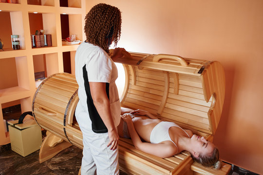 Wooden phyto barrel, horizontal sauna. Beautiful woman massage therapist applying spa treatment to a young woman in a wellness room