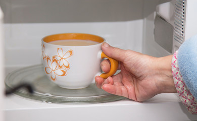 woman hand using are bringing coffe cup to the microwave oven at home. To reheat frozen food for their. Cooking made easy concept.