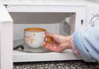 Fototapeta na wymiar woman hand using are bringing coffe cup to the microwave oven at home. To reheat frozen food for their. Cooking made easy concept.