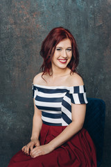 Naklejka premium Attractive bright redhaired smiling woman in striped blouse on green background