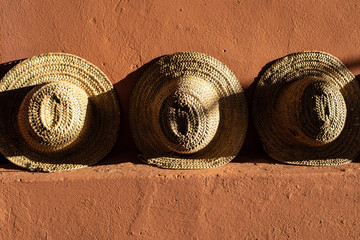 Straw beach hats standing on terracotta  clay wall.  Bright sunlight and hard shadows.