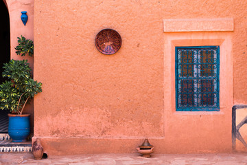 Traditional Moroccan exterior: blue forged window, brown clay Tajine, plate and flower pot in the...