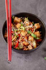 The concept of Japanese cuisine. Vegetarian noodles with tofu cheese and vegetables in a black ceramic plate. Red Chinese sticks. copy space