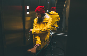 Bicycle girl in yellow raincoat pushing button in elevator