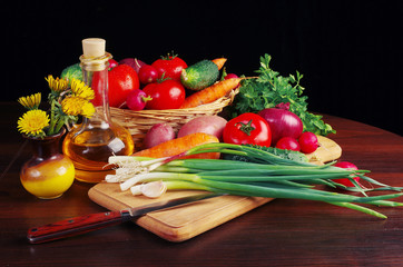 Appetizing vegetables and sunflower oil on a wooden table. Green onions, tomatoes, cucumbers, carrots, radishes, garlic, parsley.