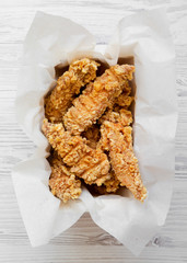 Chicken fingers in paper box on a white woodentable, top view. Flat lay, from above, overhead. Close-up.