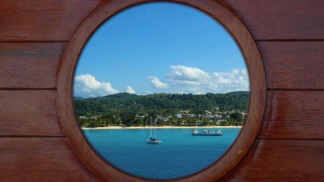 Looking outside through a porthole of a cruise ship to the beach of Jamaica