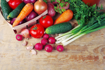 Appetizing vegetables on a wooden table. Green onions, tomatoes, cucumbers, carrots, radishes, garlic, parsley.