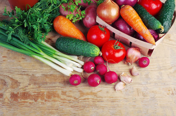 Appetizing vegetables on a wooden table. Green onions, tomatoes, cucumbers, carrots, radishes, garlic, parsley.